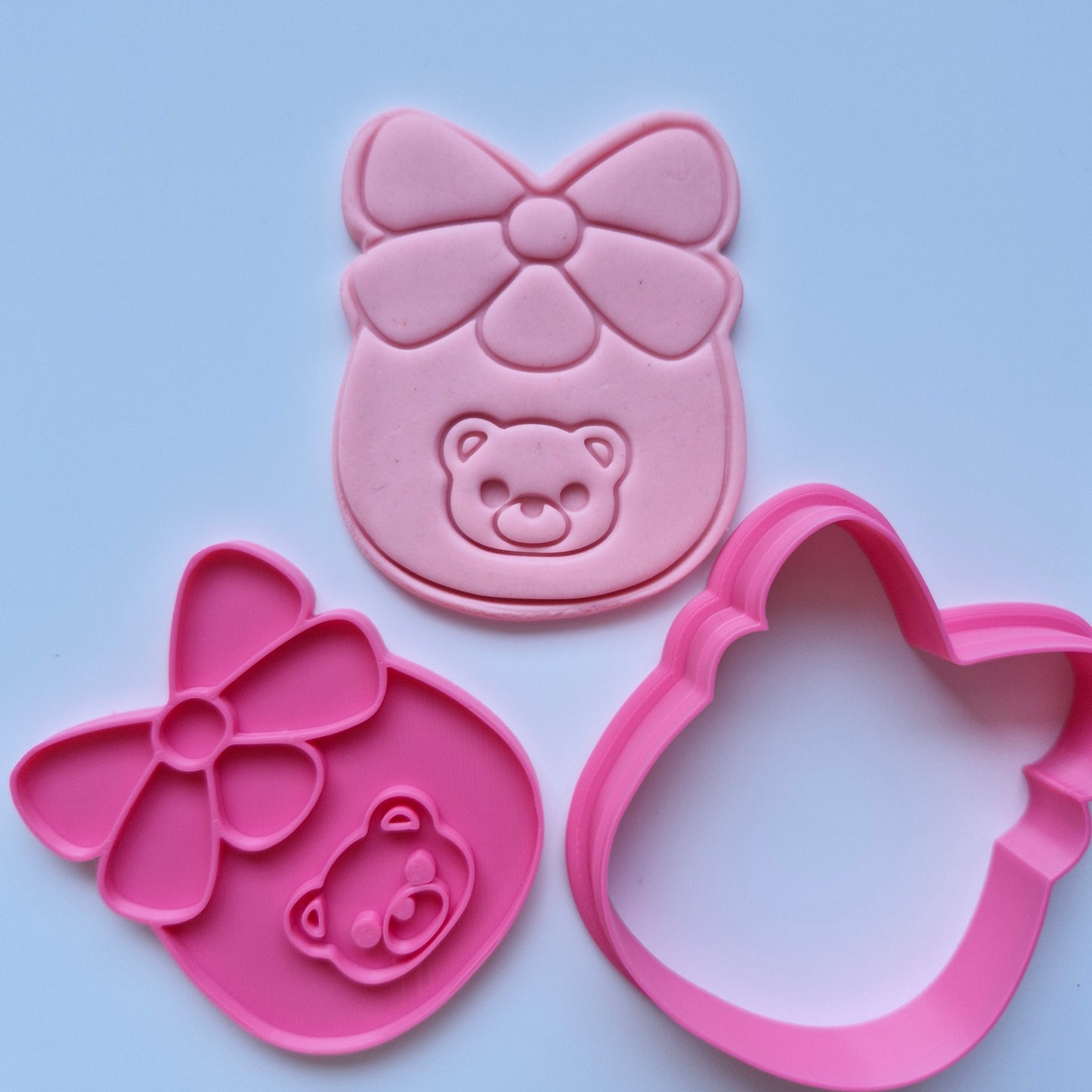 pink cookie cutter and fondant stamped with the shape of a baby bib with a bear face on it on white background Baby Bib with Bear Face Cookie Cutter and Stamp