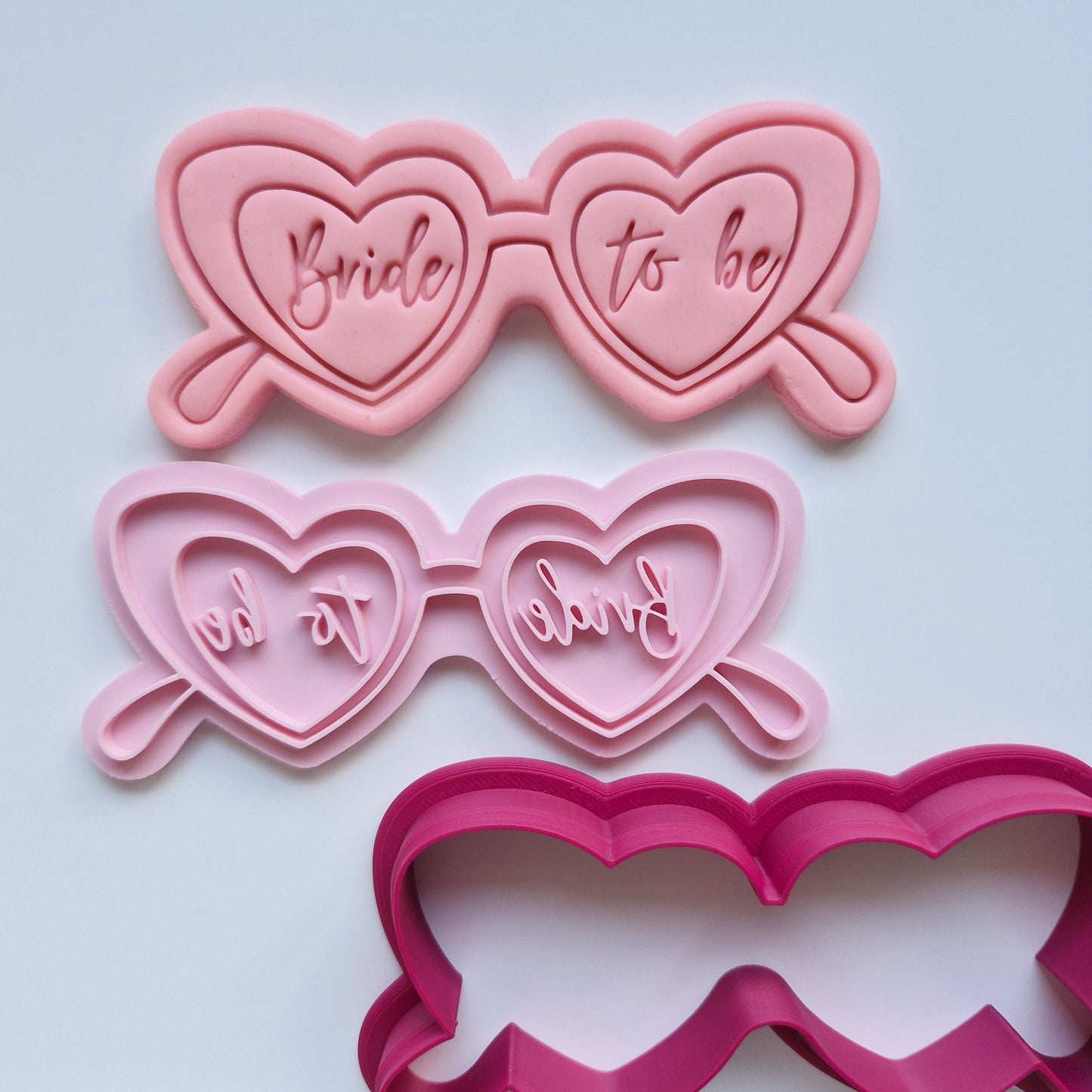 pink fondant and stamp in the shape of cat eye glasses with the writing bride to be in the lenses, cutter is read, and everything is laid out on white background Bride to Be Glasses, Cookie Cutter and Stamp