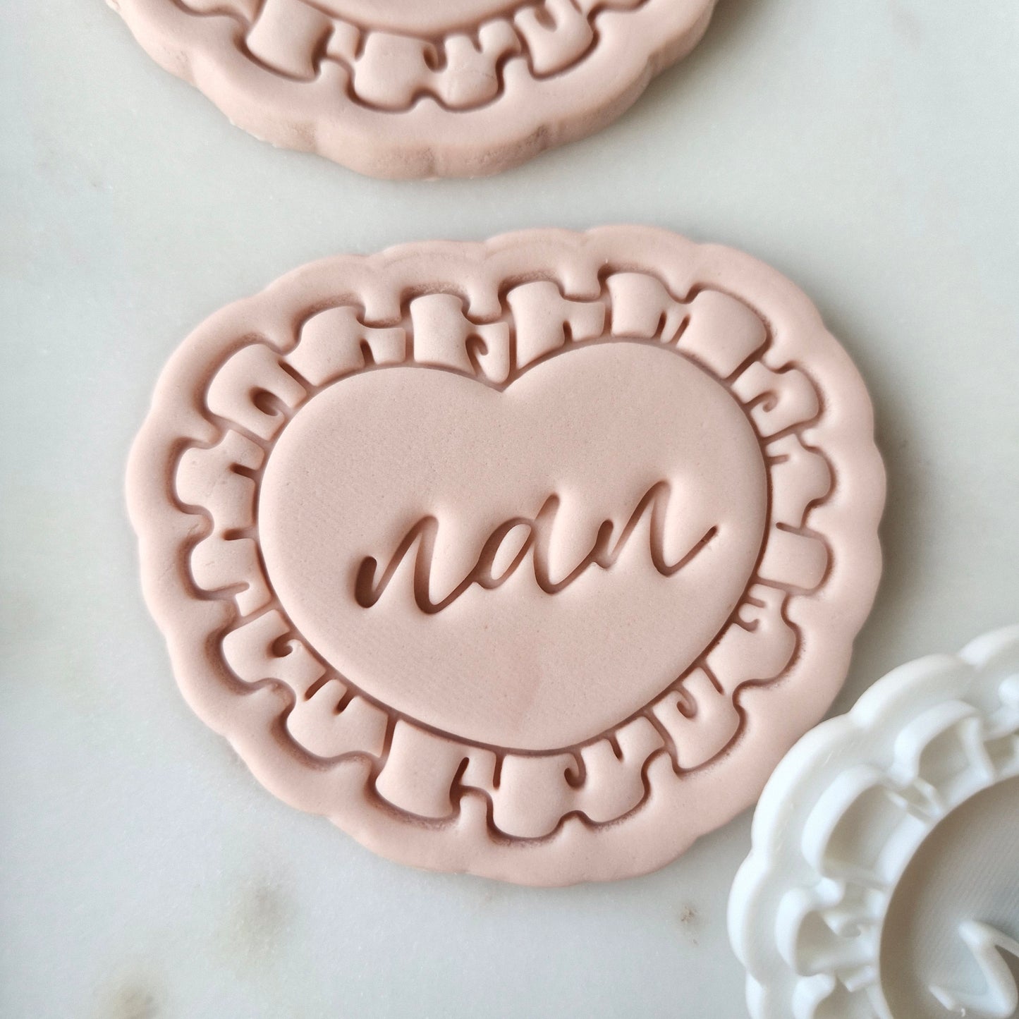 Nan on Heart with Frills Cookie Cutter and Stamp, zoomed in on the heart with writing nan in the middle, and on white marble background