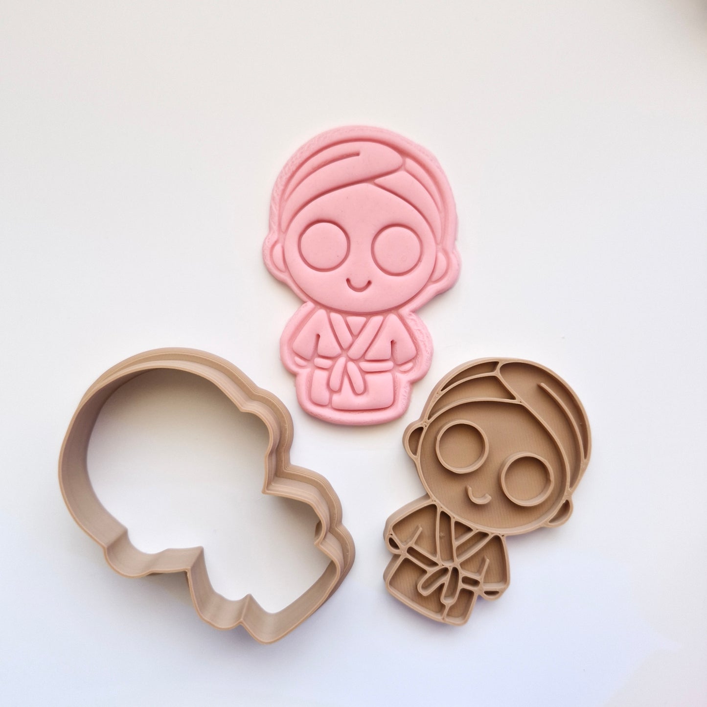 pink fondant, with brown cookie cutter and stamp, in the shape and imprint of a girl in robe with cucumbers on the eyes, on white background, zoomed out