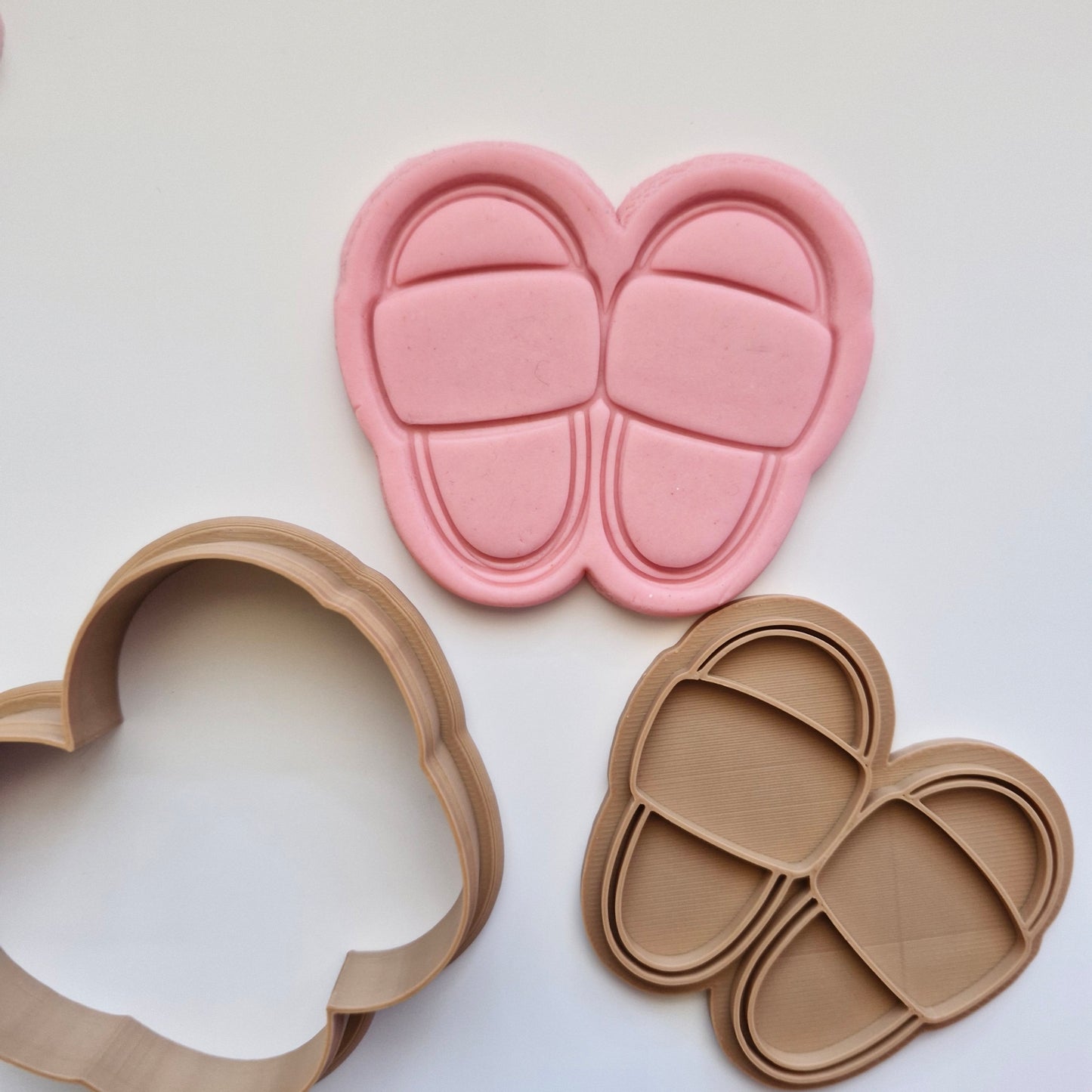 pink fondant, with brown cookie cutter and stamp, in the shape and imprint of slippers, zoomed out on white background