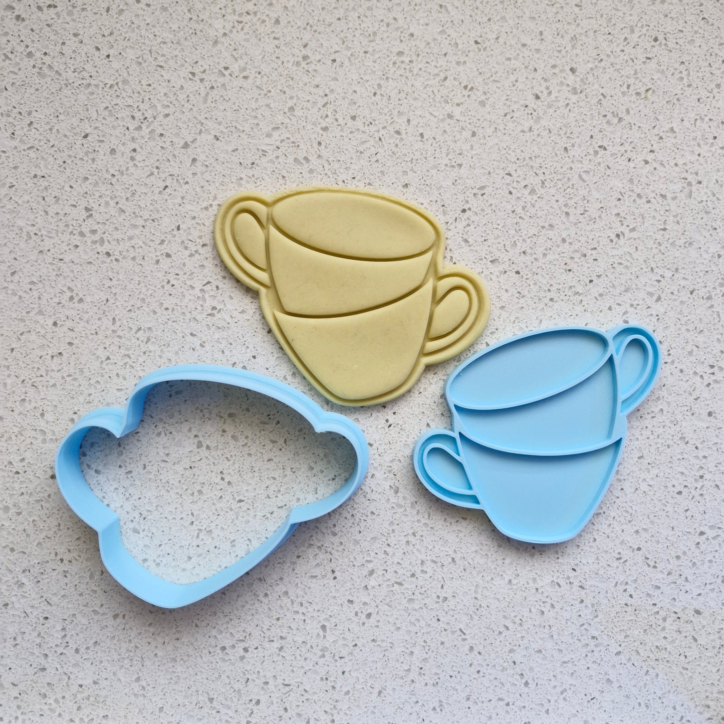 stacked teacups, in the format of yellow fondant, blue cookie cutter and stamp, on white speckled stone