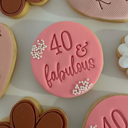 Pink cookie with '40 & fabulous' text on a white surface with other cookies.