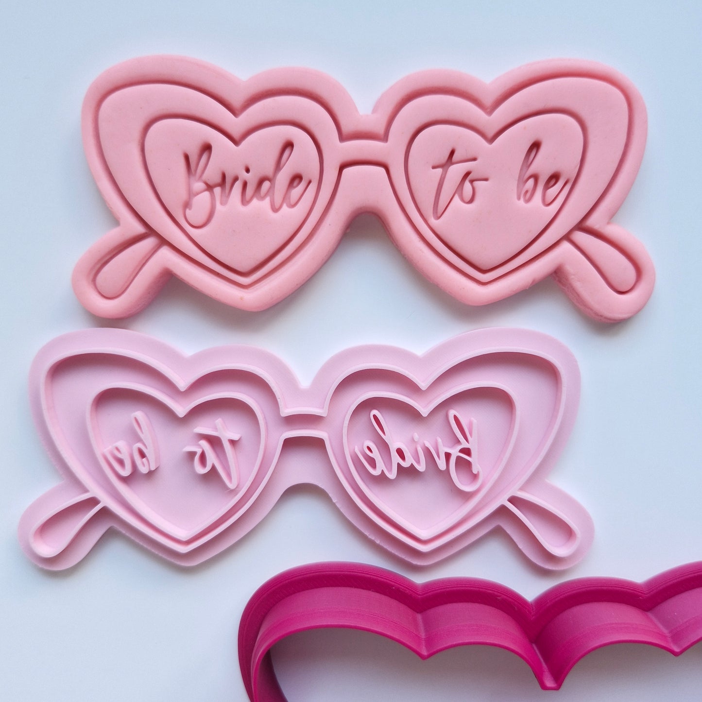 Pink cookie cutters shaped like sunglasses with heart lenses cat eye glasses with the word birde to be on them and on a white background Bride to Be Glasses, Cookie Cutter and Stamp