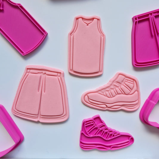 there are 3 pink fondant shapes and cut and stamped by the pink  cookie cutters and stamps making a set of 3 an activewear outfit, includes of jersey single, shorts and sneakers on white background. Activewear Outfit Set Cookie Cutter and Stamp