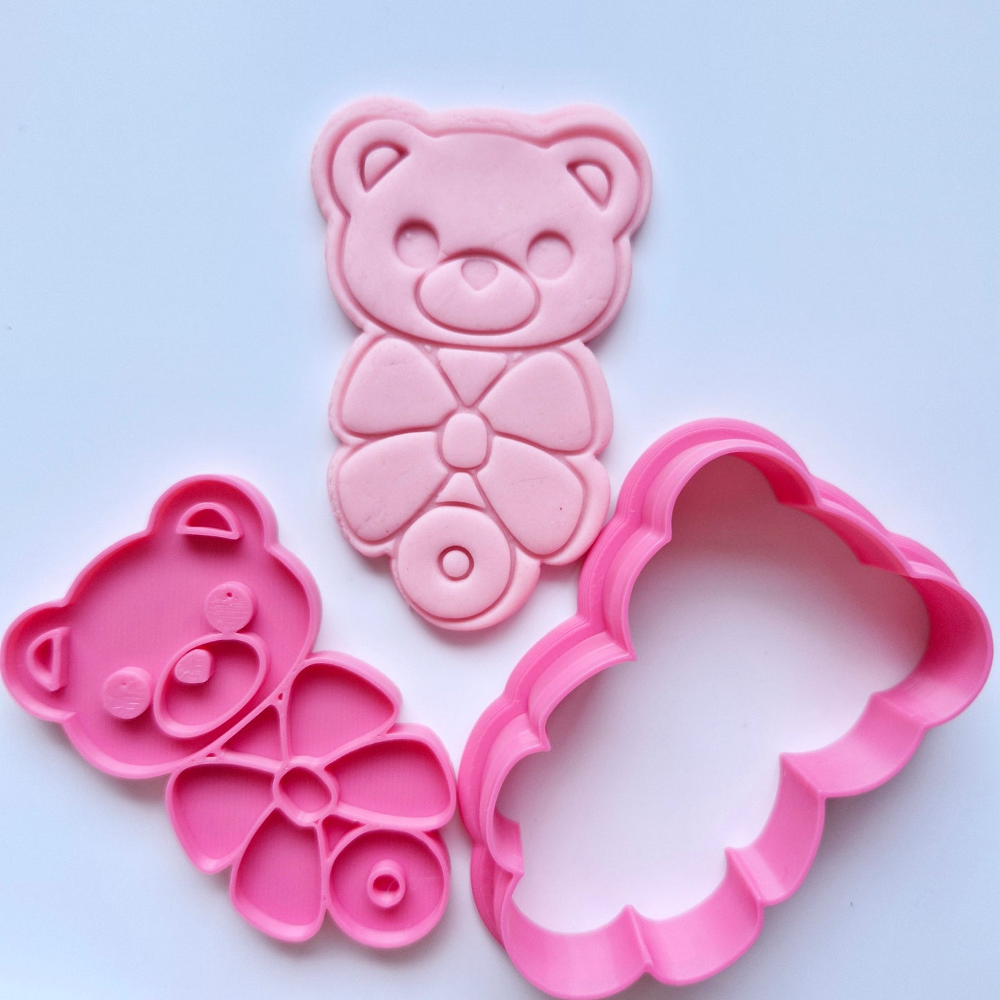 Bear Rattle With Bow Cookie Cutter and Stamp, pink cookie cutter and stamp, stamped on pink fondant with the design of a baby rattle with bear head and bow