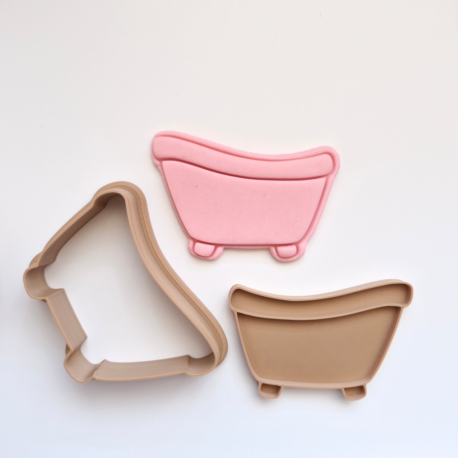 pink fondant, and brown cookie cutter and stamp in the shape and imprint of a bathtub, all on white background zoomed out
