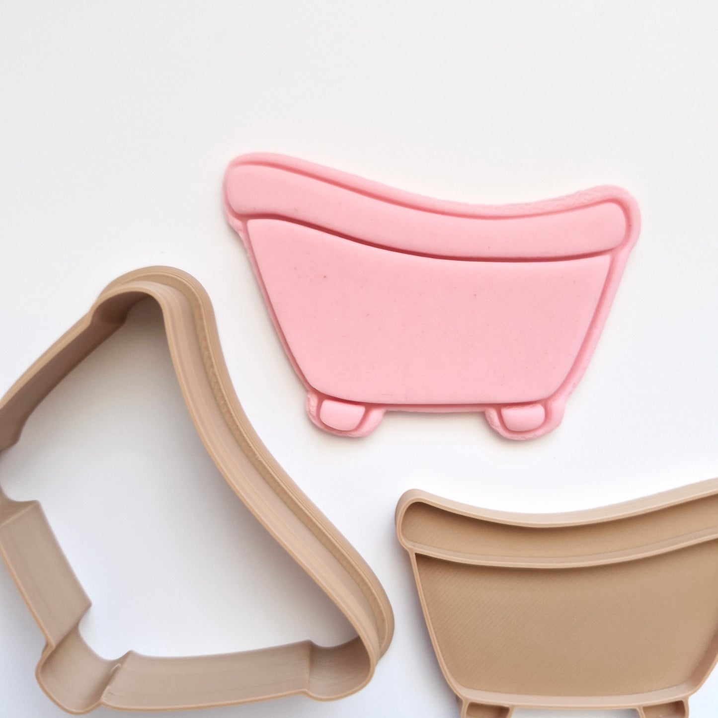 pink fondant, and brown cookie cutter and stamp in the shape and imprint of a bathtub, all on white background, zoomed in