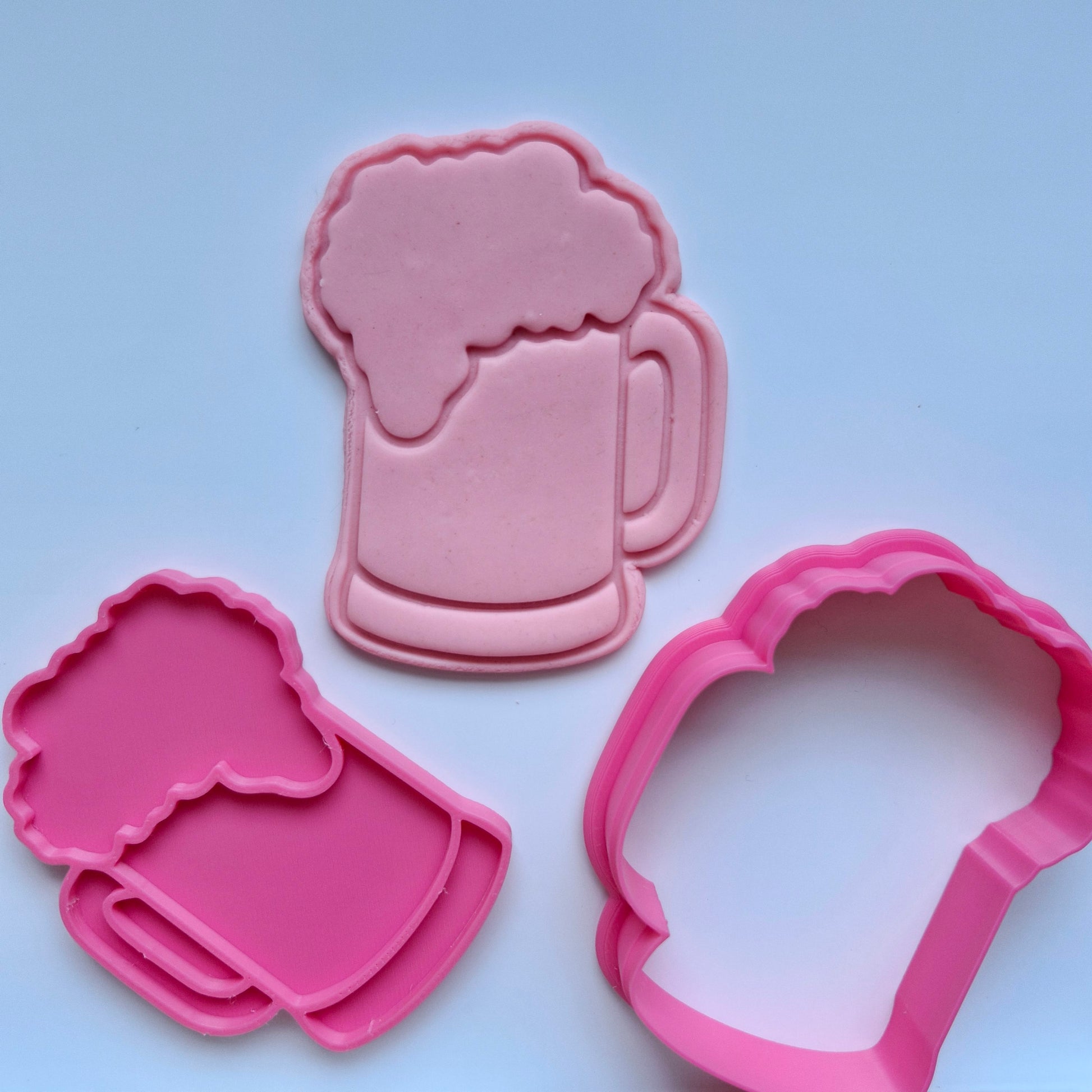 pink fondant that has been stamped and cut in the shape of plain beer glass with foam on top, cookie stamp and cutters laying flat bellow it with white background Plain Beer Mug Cookie Cutter and Stamp 