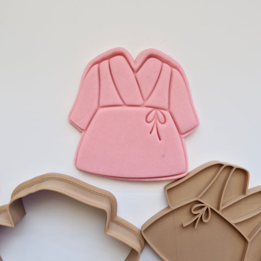 pink fondant, alongside brown cookie cutter and stamp, in shape and imprint of a simple bathrobe, zoomed in