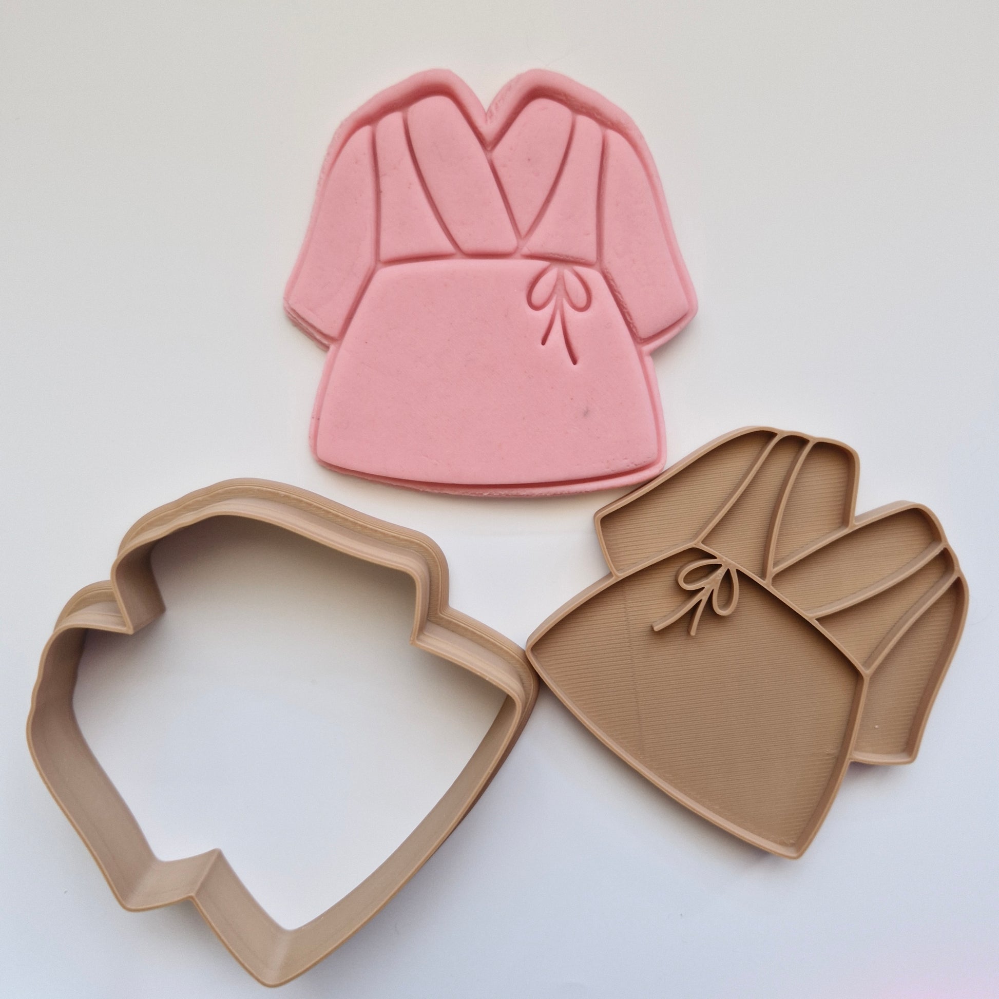 pink fondant, alongside brown cookie cutter and stamp, in shape and imprint of a simple bathrobe, zoomed out