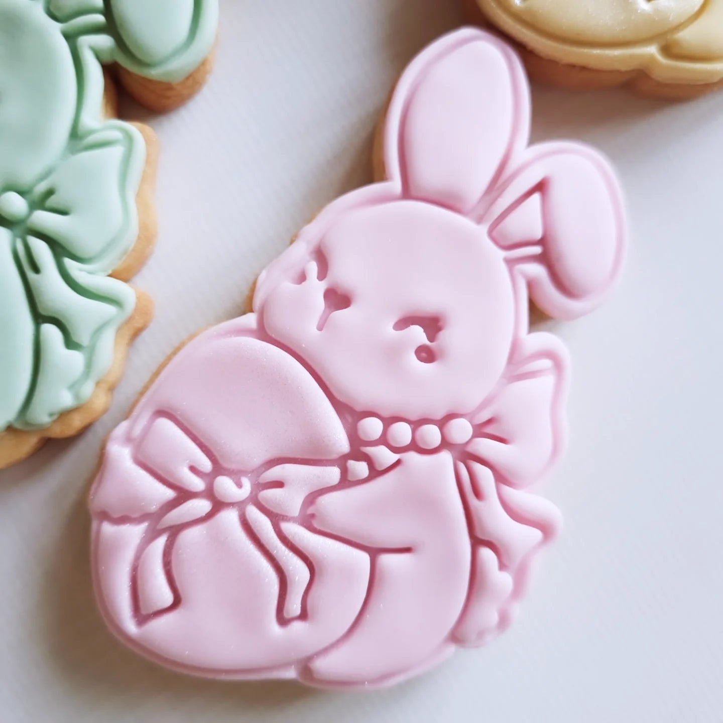 coquette bunny holding an egg wrapped in bow the bunny has a pearl necklace and bow on the back, the bunny is pink and sugar cookie Coquette Bunny Cookie Cutter and Stamp