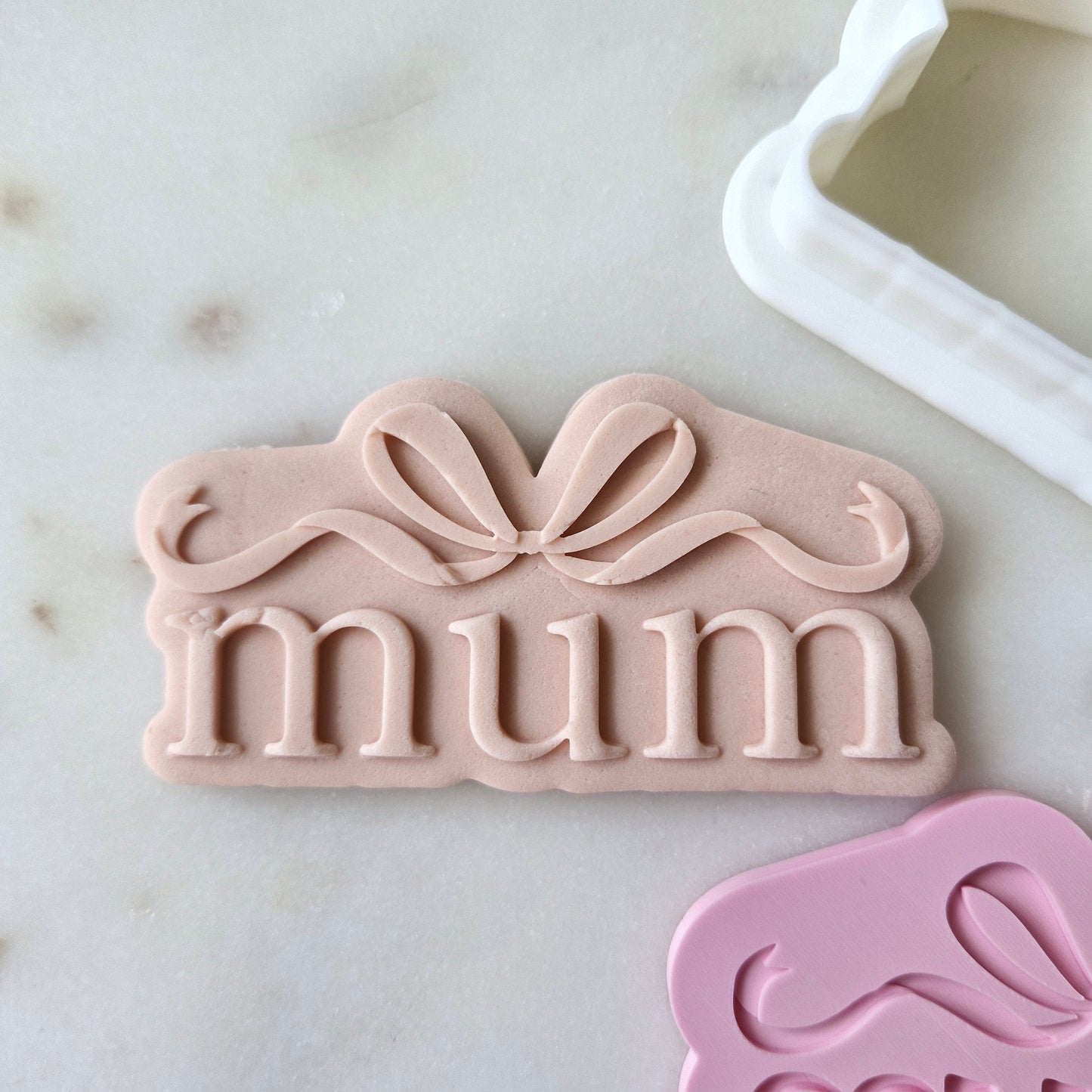 Mum With Bow Cookie Cutter and Stamp zoomed in and on white marble background