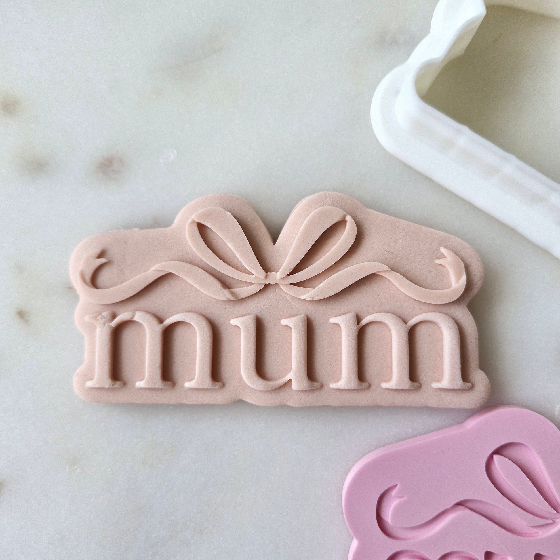Mum With Bow Cookie Cutter and Stamp zoomed in and on white marble background