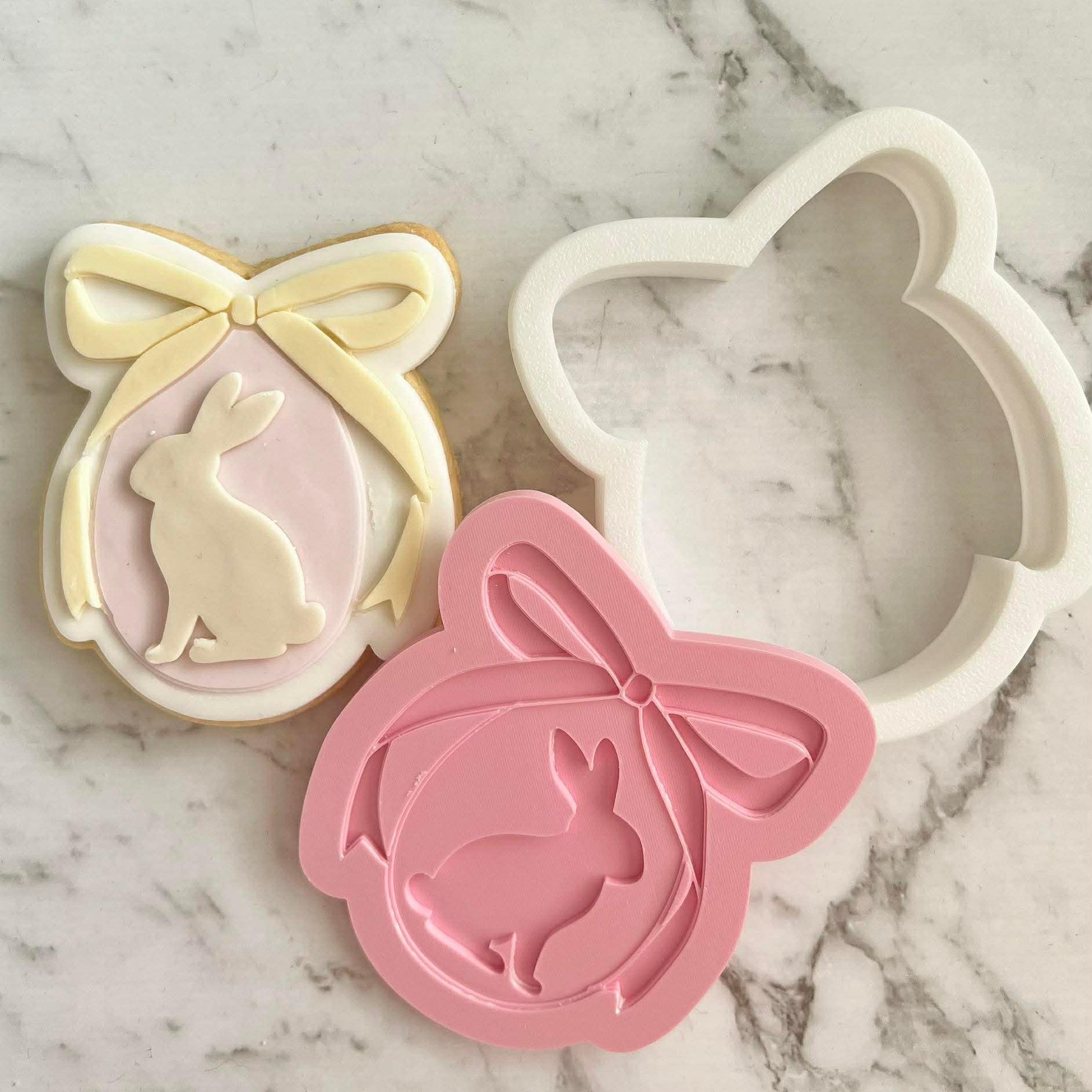 sugar cookie with two tone fondant, in the shape cookie cutter cutter and stamp in the shape of a coquette egg with a bunny inside the egg and a bow on top