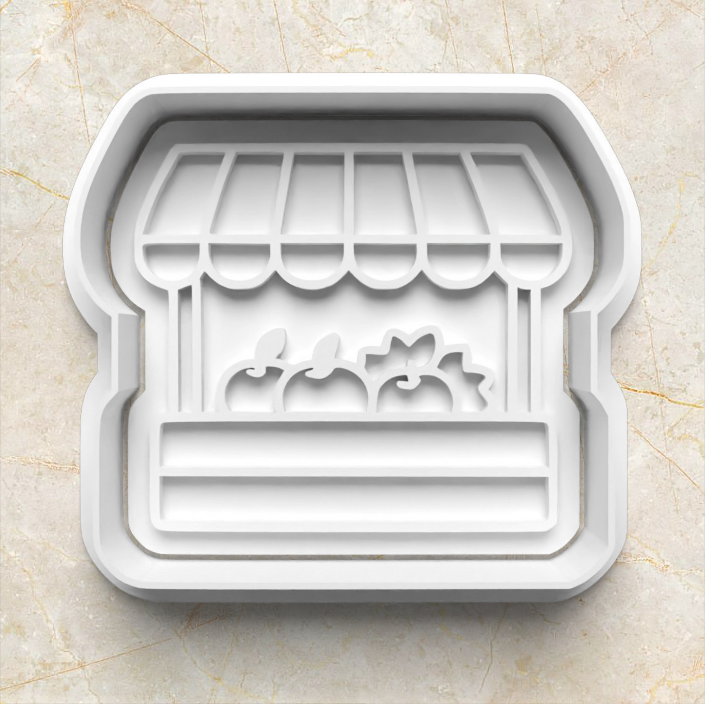 Decorative cookie cutter shaped like a store front with an awning on a beige marble background. Farmer's Market Cookie Cutter and Emboss Stamp