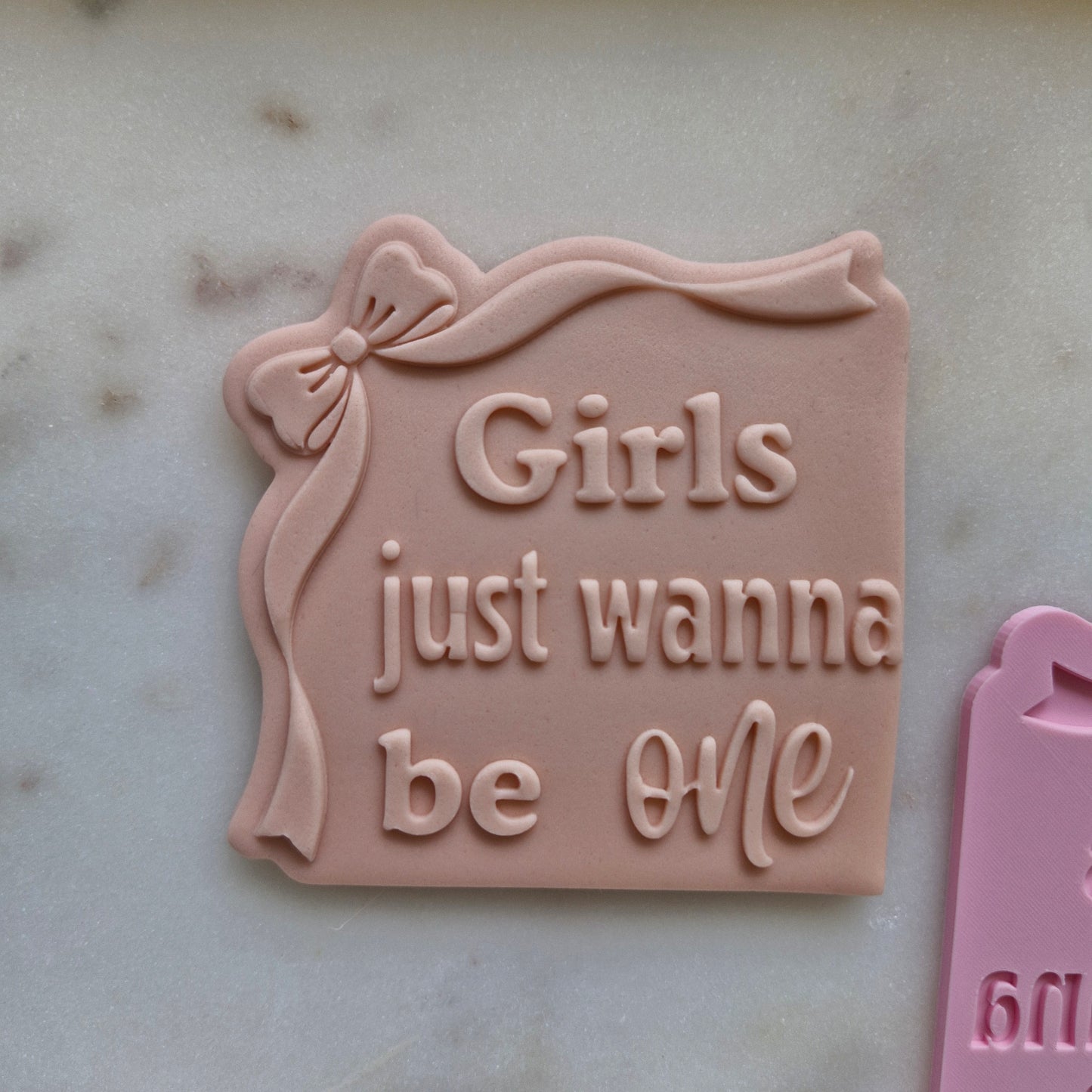 Girls Just Wanna be One Cookie Cutter and Stamp deboss stamped on beige fondant, with white marble background zoomed in 