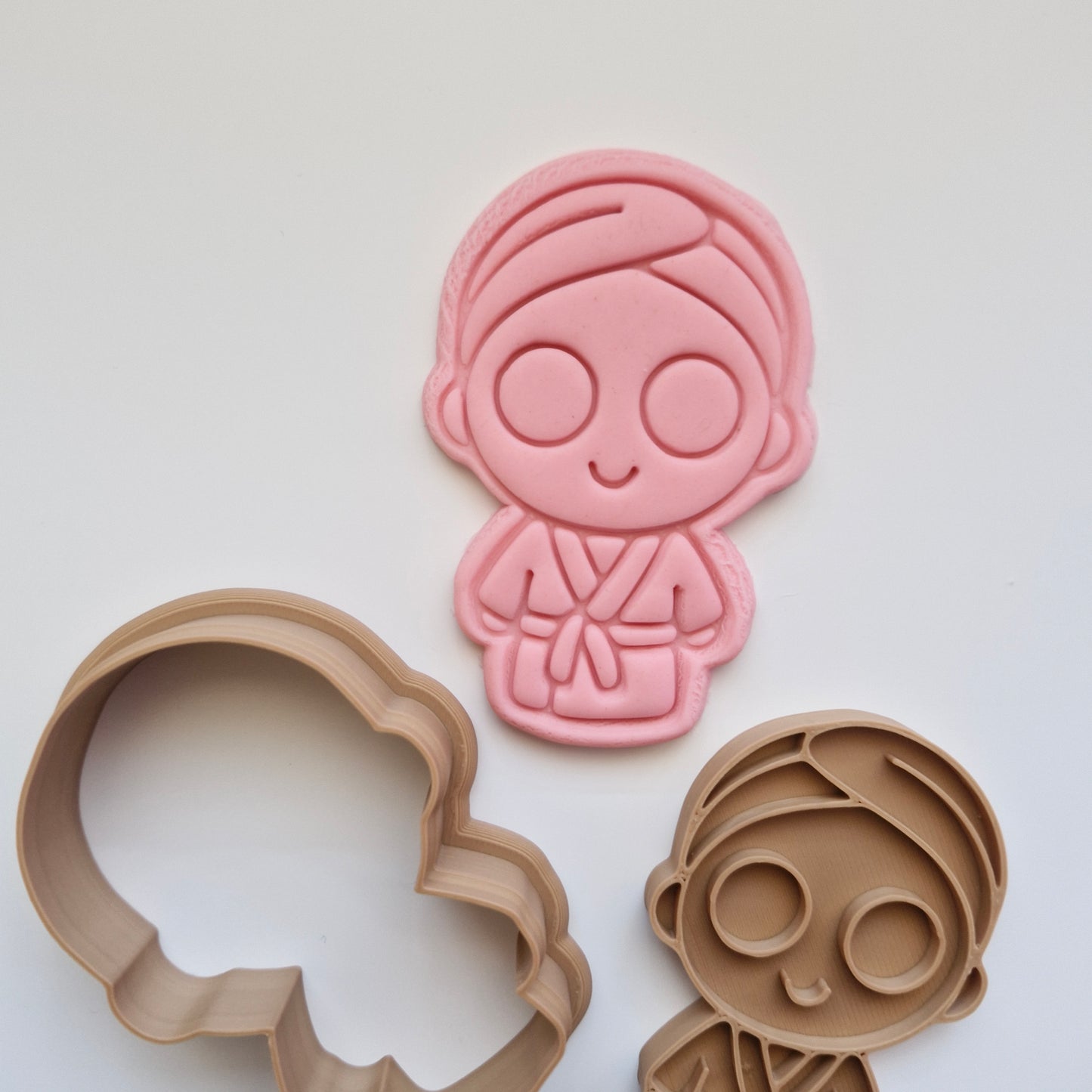 pink fondant, with brown cookie cutter and stamp, in the shape and imprint of a girl in robe with cucumbers on the eyes, on white background, zoomed in