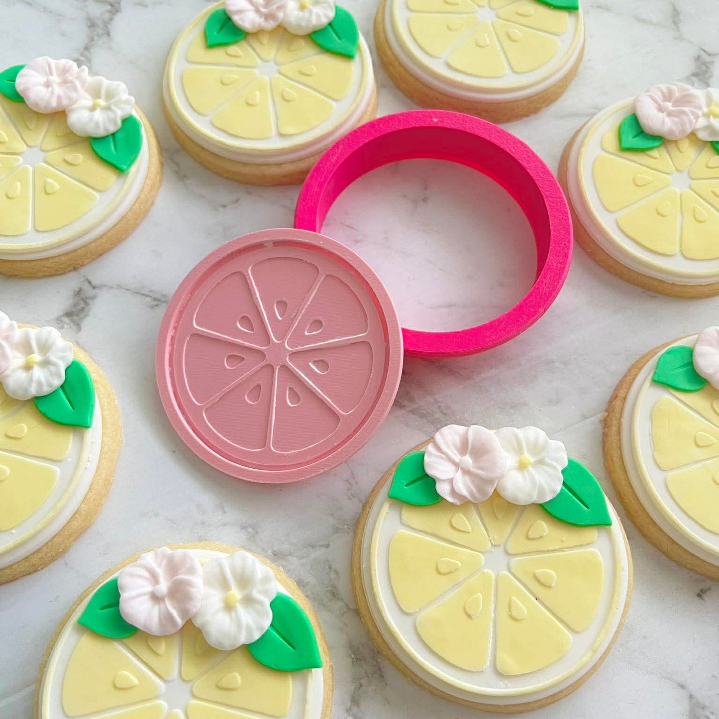design of a lemon cut in half, of a sugar cookie and stamp, surrounded by lemon fondant cookies around it, on marble background
