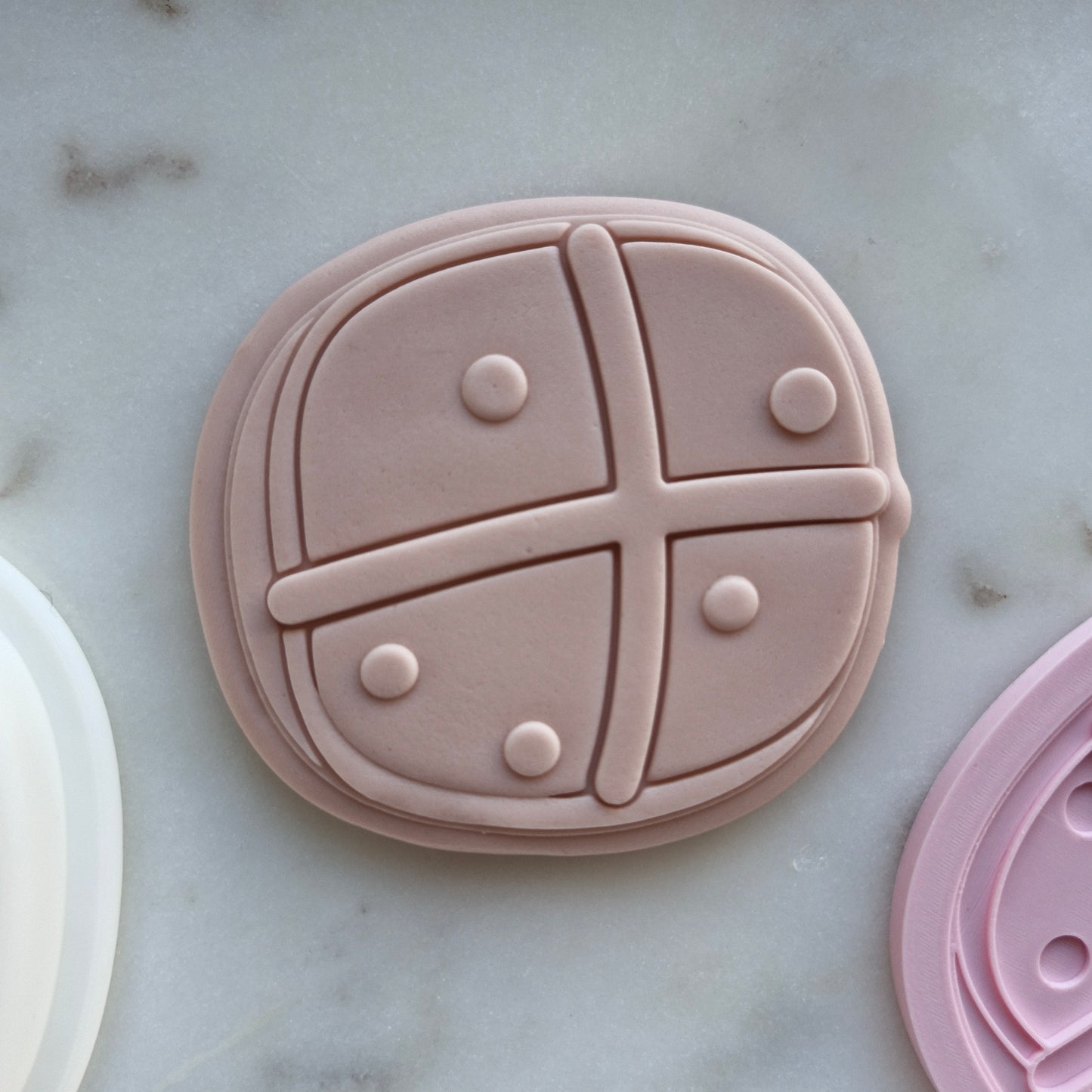 hot cross bun, stamped on beige fondant, flat on white marble alongside cookie stamp and cutter