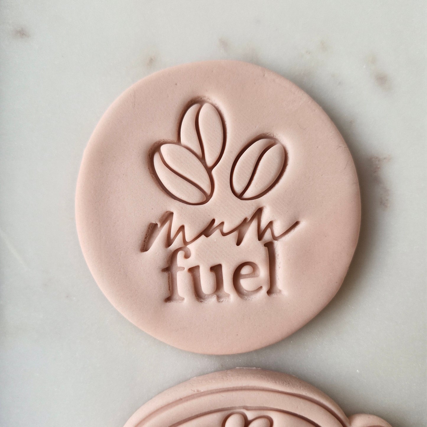 Mum Fuel Set Cookie Cutter and Stamp zoomed in on the stamp that says mum fuel and has images of coffee beans on it, on white marble background