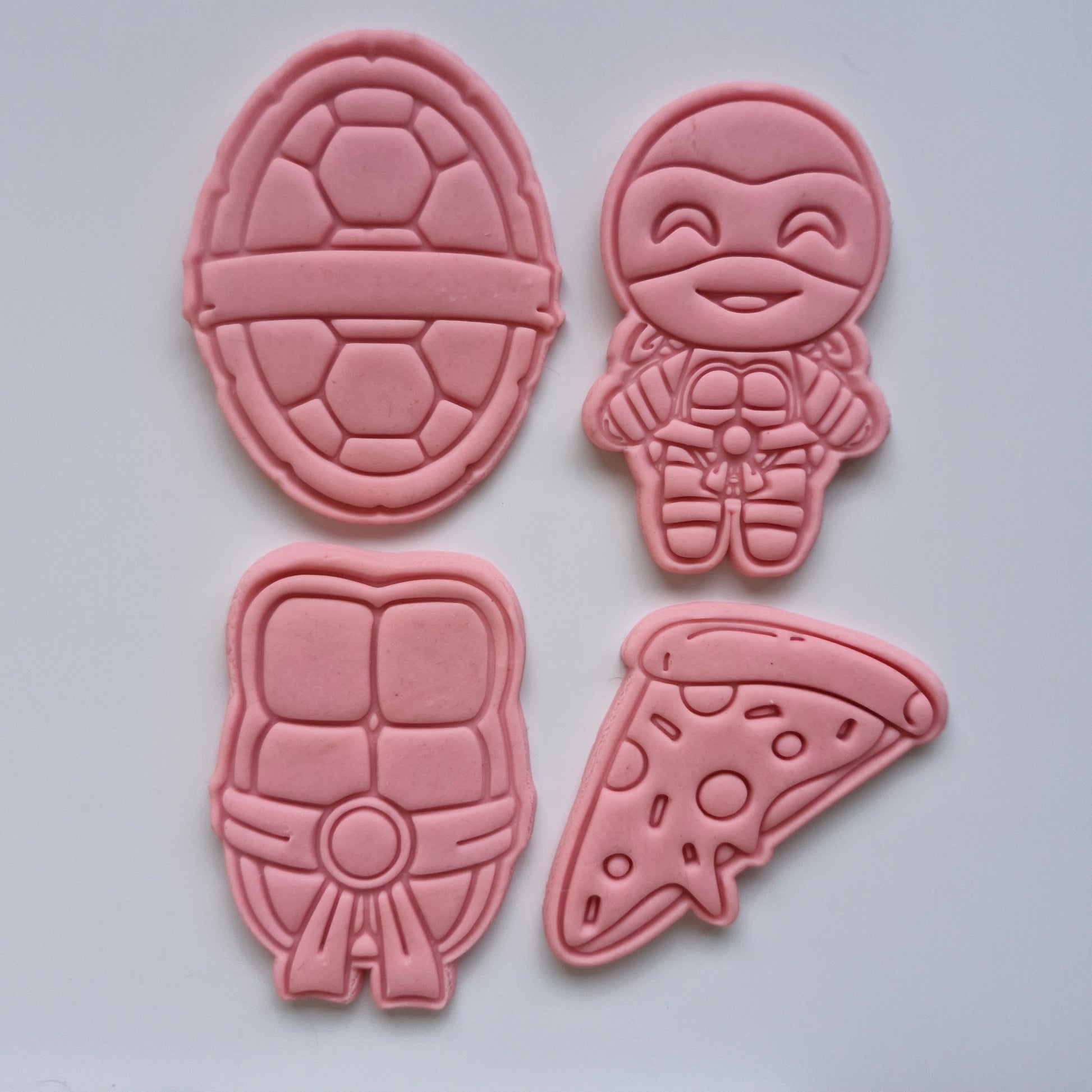 4 pink fondant stamped and cut in by the shapes of ninja turtle, ninja shell, pizza, turtle abs