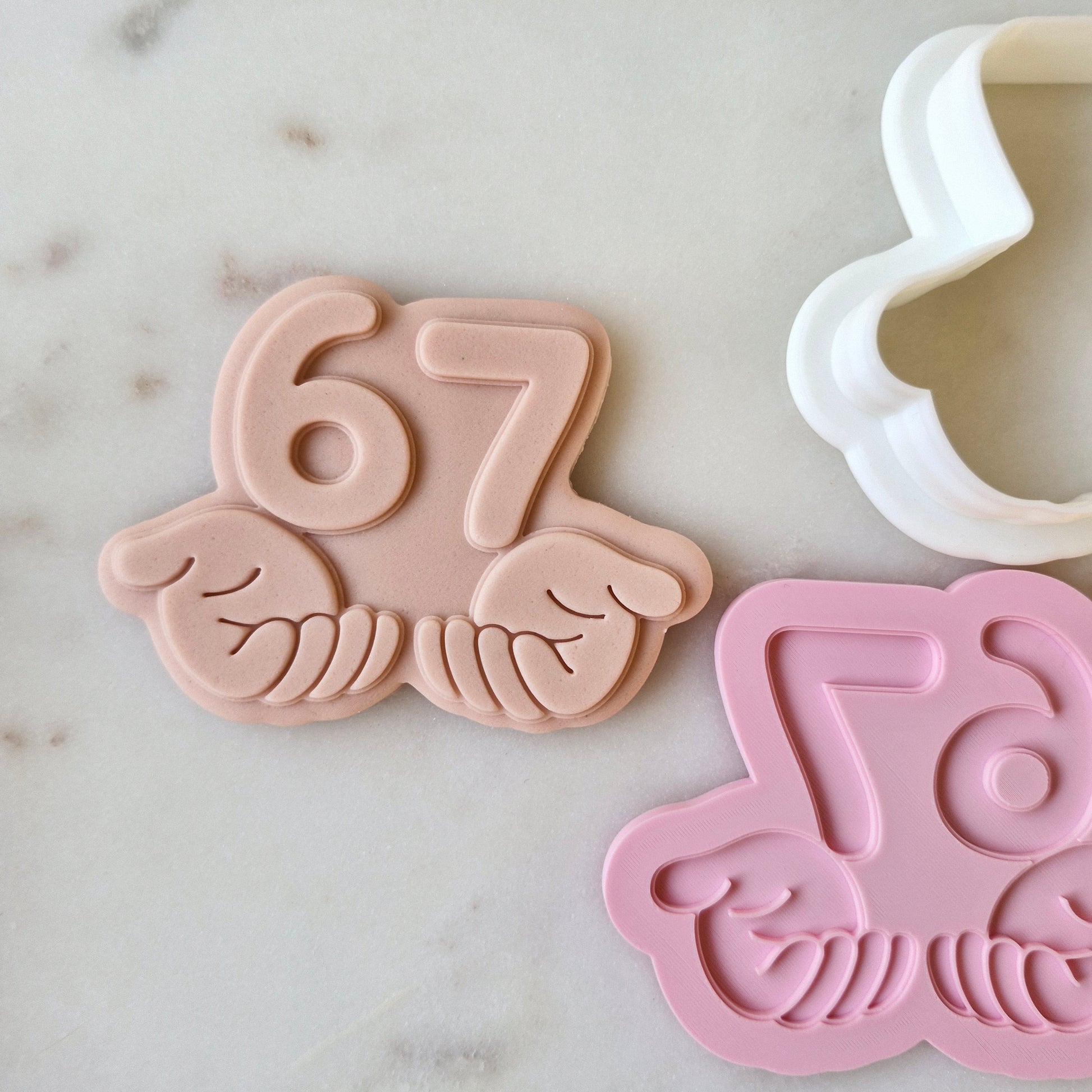Six Seven 6 7 Cookie Cutter and Deboss Stamp numbers help in hands on white marble background zoomed out