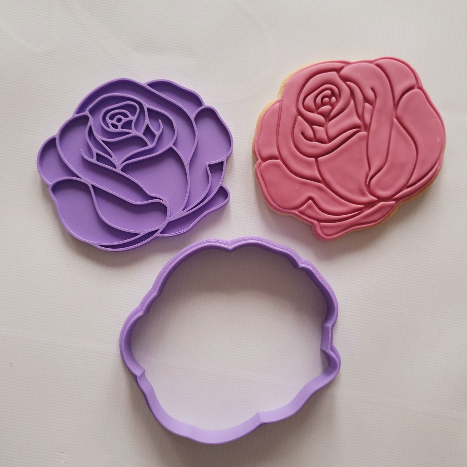 rose flower cookie cutter and stamp, alongside sugar cookie in red on white background