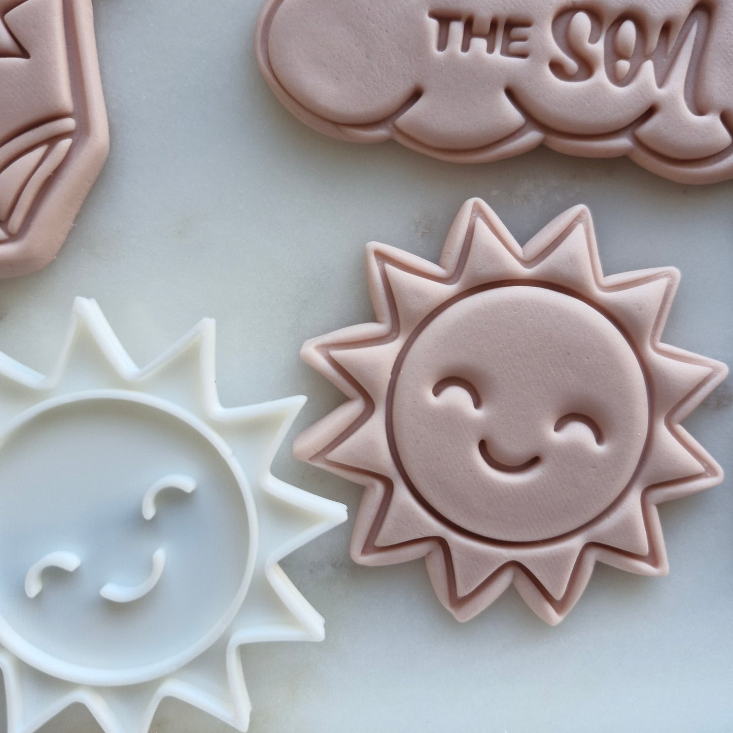 Here Comes the Son Set Cookie Cutter and Stamp Baking Tool sun-shaped cookie and fondant designs on marble surface.Here Comes the Son Set Cookie Cutter and Stamp Baking Tool